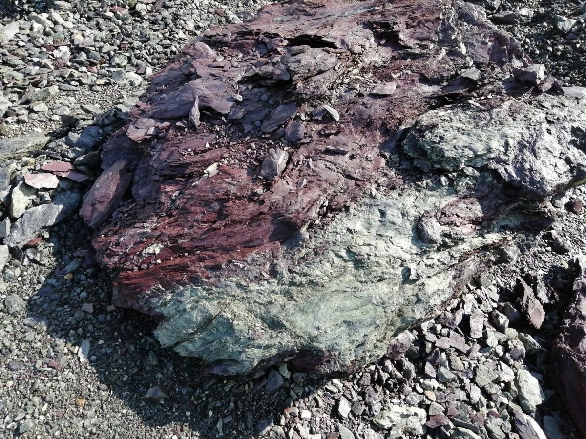 Gesteinsblock im Steinbruch: unten grüngrauer Grünstein, darüber rotviolette vulkanische Aschen