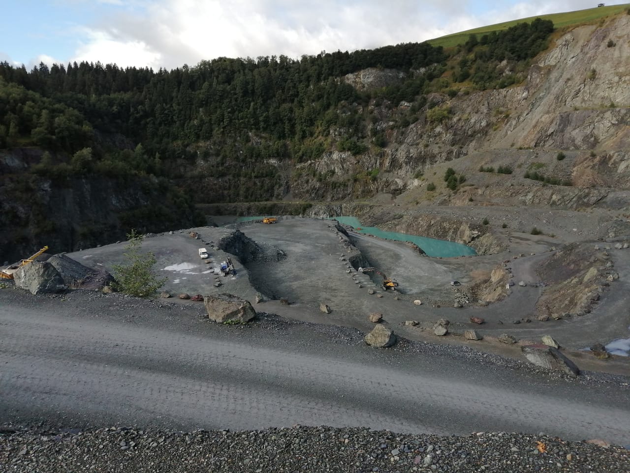 Der Steinbruch des Hartsteinwerks Kitzbühel: terrassierte Abbauwände aus grüngrauem Vulkangestein, in der Sohle ein türkisfarbener Wasserspiegel