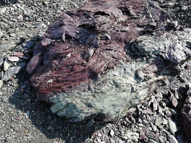 Gesteinsblock im Steinbruch: unten grüngrauer Grünstein, darüber rotviolette vulkanische Aschen